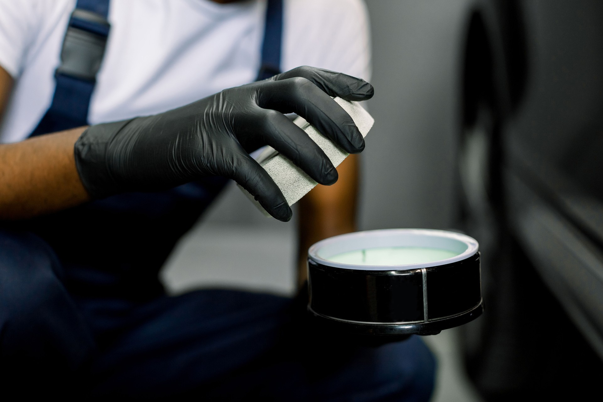 Car detailing, tools for polishing. Professional auto care products. Cropped close up shot of worker hands in gloves, holding the jar with solid carnauba wax to polish the car body